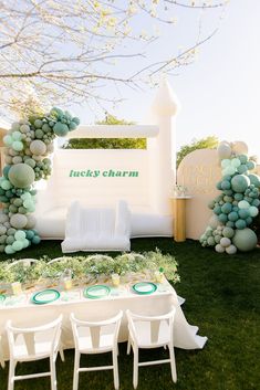 a table set up for an event with balloons and greenery on the grass, surrounded by chairs