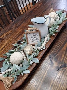 a wooden table topped with a tea pot and greenery next to a sign that says gather grateful hearts