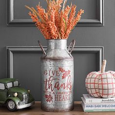 a metal can with flowers in it sitting on a table next to books and pumpkins