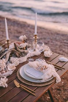 a table set up on the beach for an outdoor dinner with candles and napkins