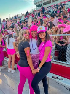 two women in pink hats and black pants posing for a photo at a sporting event