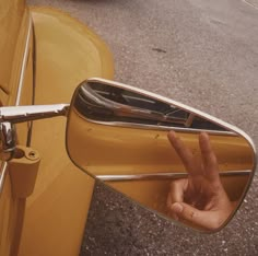 a person's hand sticking out the side mirror of a yellow car