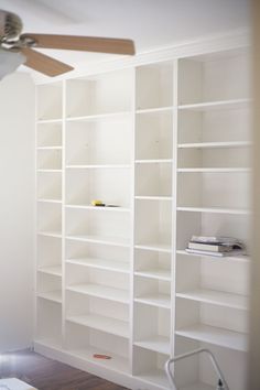 an empty room with white bookcases and ceiling fan