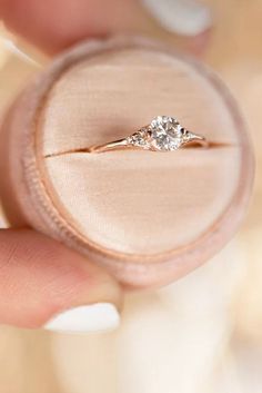 a close up of a person's hand holding an engagement ring in a velvet box