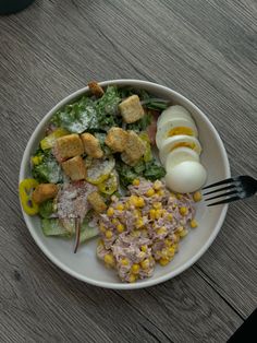 a white plate topped with salad next to an egg on top of a wooden table