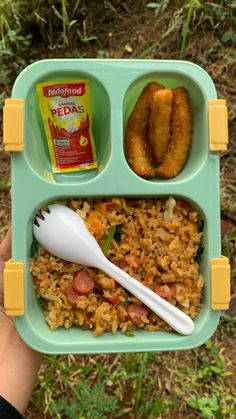 a child's hand holding a tray with rice, sausages and other food