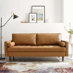 a tan leather couch sitting on top of a rug next to a white vase and lamp