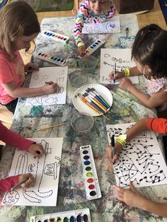 three children are sitting at a table with art supplies and coloring paper on it while one child is drawing