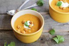 two yellow bowls filled with soup and garnished with green leafy leaves on top