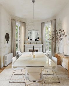 a white dining room table surrounded by chairs and tables with windows in the back ground