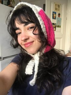 a woman wearing a knitted hat and scarf in front of an open refrigerator door