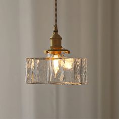 a clear glass light fixture hanging from a metal ceiling hook in a white walled room