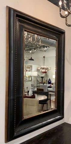 a large mirror hanging on the wall above a dining room table with chairs and a chandelier