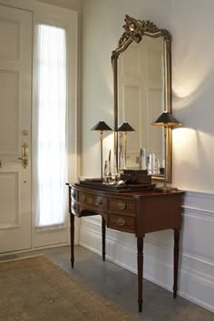 an antique desk with two lamps and a mirror on it in front of a door