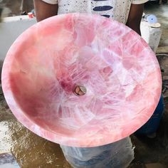 a person holding a large pink bowl in their hands and some water on the ground