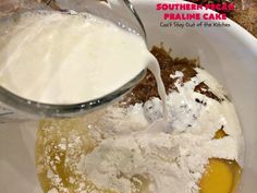 someone pouring milk into a bowl filled with flour and other ingredients for making cake mix