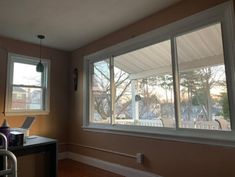 an empty room with two windows and a laptop on the desk in front of it