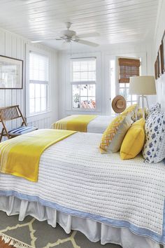 two beds in a room with white walls and yellow pillows on the bed, one has a hat on top of it