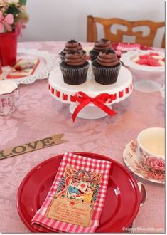 cupcakes are sitting on top of plates with red ribbon around them and pink table cloth