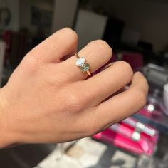 a person's hand holding a ring with a diamond on it and the other hand