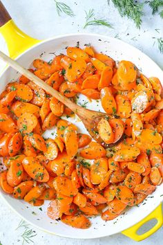 a white bowl filled with sliced carrots and parsley next to a wooden spoon