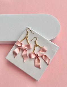 the pink bow earrings are on display in front of a white box with gold chains