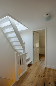 an empty room with white walls and wooden flooring on the bottom level has a staircase leading up to the second floor