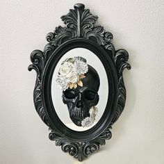 a mirror with a skull and flowers in the middle is hanging on a white wall