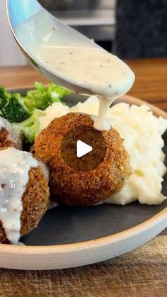 a plate with meatballs, mashed potatoes and broccoli is being drizzled with sauce