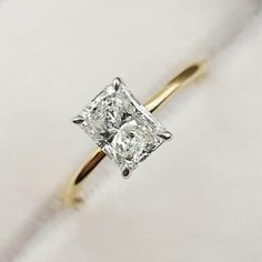 an engagement ring with a princess cut diamond on it's side, sitting on a white cloth