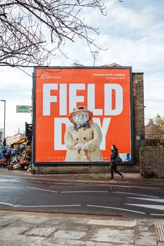 an orange field day advertisement on the side of a building with a woman walking past it