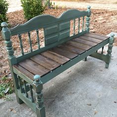 a green bench sitting on top of a cement ground next to a tree and bushes