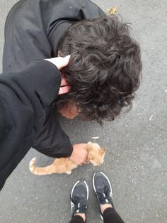 a person is petting a small cat on the street while wearing black pants and sneakers