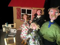 three dolls are standing in front of a doll house with a man and two women