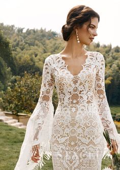 a woman in a white wedding dress with long sleeves and an intricate lace pattern on it