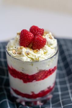 a dessert with raspberries and whipped cream in a small glass dish on a table