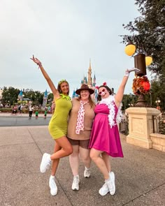 three women in costumes posing for a photo at disney world with their arms up and hands raised