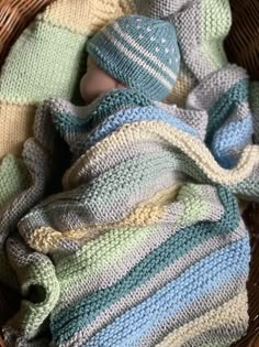 a knitted baby wrapped in a blue and green striped blanket sitting in a wicker basket