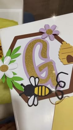 a close up of the letter g on a sign with bees and flowers in it