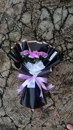 a bouquet of flowers is wrapped in black paper and tied with pink ribbon on the ground