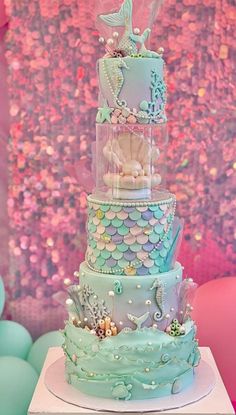 a three tiered cake is decorated with blue and green mermaids, pearls, and seahorses