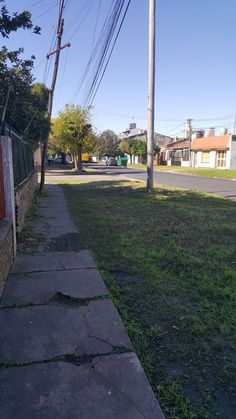 an empty sidewalk next to a street with power lines in the background and houses on the other side