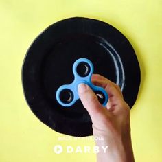 a hand holding a blue pair of scissors over a black plate on a yellow background