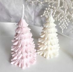 two white and pink christmas trees sitting next to each other on top of a table