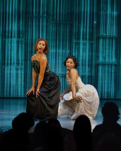 two women in evening dresses on stage with one woman kneeling down and the other standing up