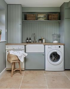 a washer and dryer in a small room with grey walls, tile flooring and wooden shelves