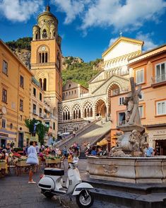 a scooter parked in front of a fountain with people sitting at tables around it