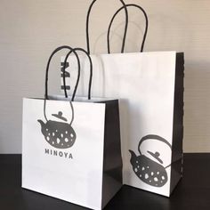 two bags with teapots on them are sitting on a black table and one bag has the word minoya printed on it