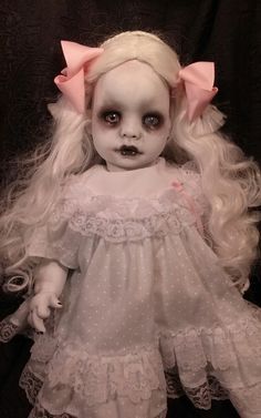 a creepy doll with long blonde hair wearing a white dress and pink bow on her head