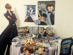 an anime themed table is set up in front of posters and other items on the wall